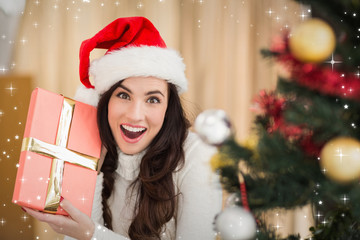 Surprised brunette holding a gift  against twinkling stars