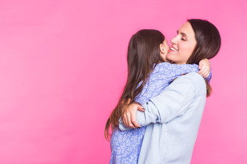 people, happiness, love, family and motherhood concept - happy little daughter hugging and kissing her mother over pink background with copyspace