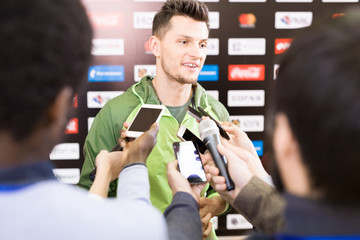 Portrait of handsome young sportsman giving interview to group of journalists during press...