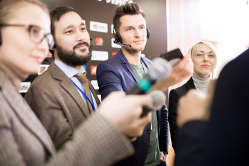 Group of cheerful journalists asking questions during press conference, taking interview