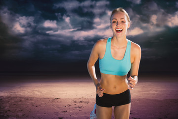 Fit woman smiling and jogging  against dark cloudy sky
