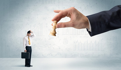Little businessman is afraid to make the next step in his chess game with graphs, charts and...
