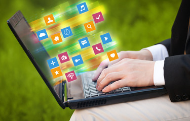 Hand using laptop with colorful fast moving application icons and symbols concept
