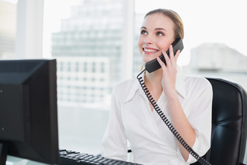 Smiling businesswoman sitting at desk on the phone