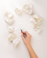 Female hand trying to write next to a few crumpled paper balls 