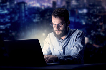 Young handsome businessman working late at night in the office with blue lights in the background