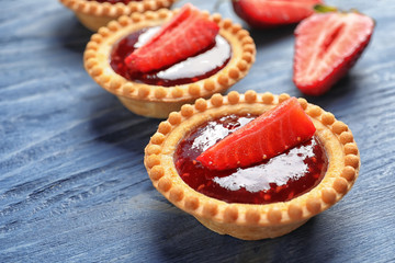 Tasty tartlets with strawberry jam on wooden background