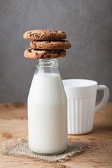 Bottle with milk and chocolate chip cookies on dark background