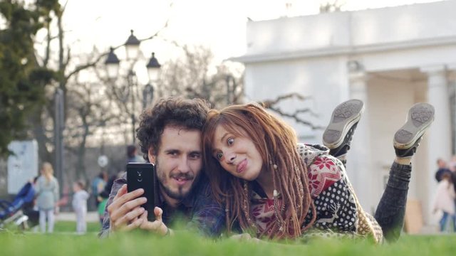 Young couple with photo camera relaxing and having fun on the green grass, dating in the summer park 