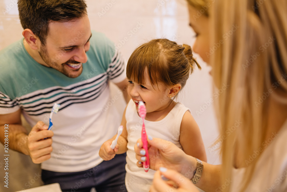 Wall mural Young parents are showing to their daughter the best way to brush teeth