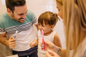 Young parents are showing to their daughter the best way to brush teeth