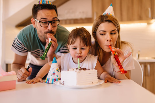 Cute little girl is having little birthday party with her parents and she is blowing candle on a birthday cake