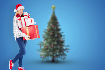 Festive blonde holding pile of gifts against blurry christmas tree