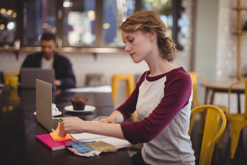 Fototapeta premium Confident female designer sitting with notebooks and papers at coffee shop