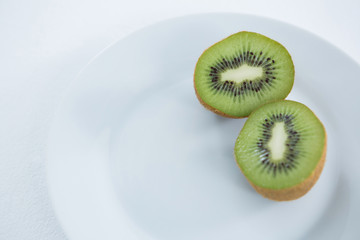 Halved kiwis in plate on white background