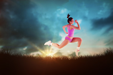 Fototapeta na wymiar Fit brunette running and jumping against blue sky over grass