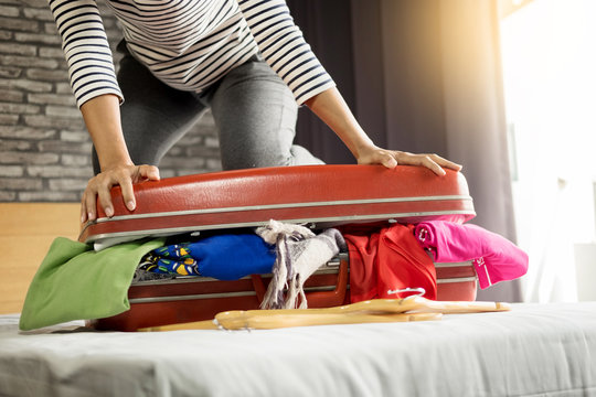 Woman trying to fit all clothing to packing her red suitcase before vacation.