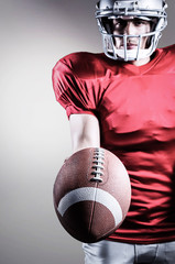 Sportsman showing American football against grey background