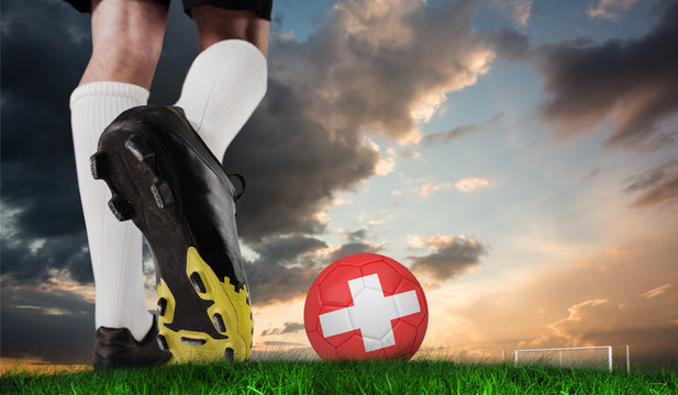 Composite image of football boot kicking swiss ball against green grass under blue and orange sky