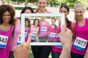 Composite image of hand holding tablet pc showing photograph of breast cancer activists