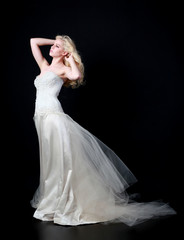 full length portrait of woman wearing white bridal gown. standing poison black studio background.