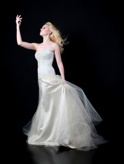 full length portrait of woman wearing white bridal gown. standing poison black studio background.