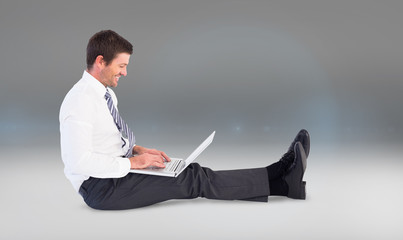 Businessman using laptop and smiling against grey vignette