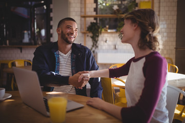 Smiling young friends shaking hands while sitting with laptop