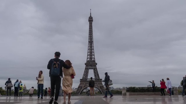 PARIS, FRANCE - SEPTEMBER 29, 2017: Timelapse shot of tourists at the city viewing point. They looking at Eiffel Tower and taking pictures with famous landmark against overcast sky. The most-visited