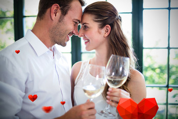 Hearts against couple looking face to face and toasting wine glasses
