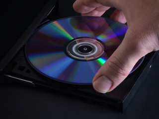 A closeup view is shown of a hand loading a DVD disc into an optical media player.