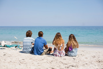 Rear view of friends sitting on during sunny day