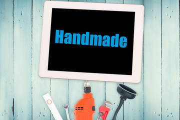 The word handmade against tools and tablet on wooden background