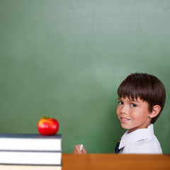 Red apple on pile of books against cute pupil holding chalk
