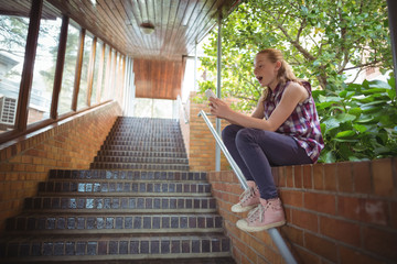 Schoolgirl sitting on brick wall and using mobile phone