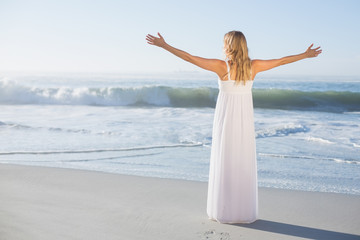 Fototapeta na wymiar Blonde standing at the beach in white sundress with arms out