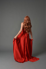 Fototapeta premium full length portrait of woman wearing red silk gown, on grey studio background.