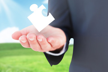 Mid section of a businessman with hands out against blue sky over green field