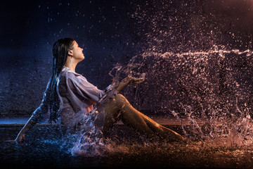 Girl in the white shirt with water drops and dark walls background illuminated by light during a photoshoot with water
