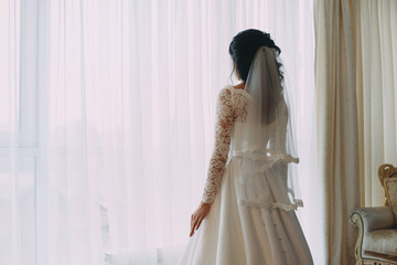 Woman by the window. Bride looking out the window, she waits for the groom. A bridal bouquet lies on the sofa. Indoors