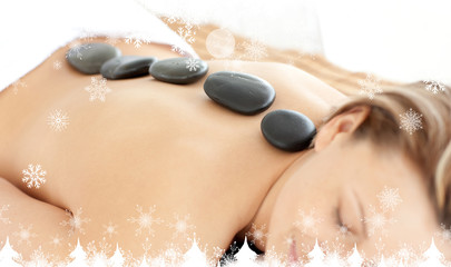 Composite image of a Relaxed woman with hot stones on her back  against snowflakes