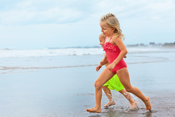 Happy barefoot kids have fun on sunset beach walk. Run by water pool along sea surf and jump with splashes. Family travel lifestyleб swimming activities. Summer vacation with child on tropical island