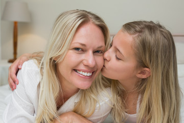 Girl kissing mother on cheek in bed