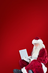 Santa sits and uses a laptop against red background