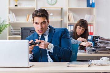 Man playing games in office while colleague is busy