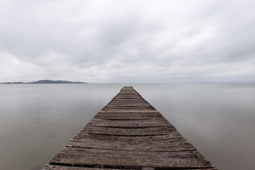 Fototapeta na wymiar Long exposure first person view of a pier on a lake with perfectly still water