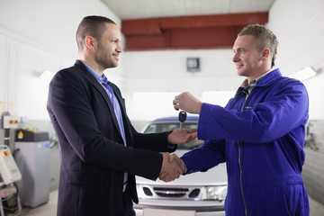Man receiving car key while shaking hand to a mechanic