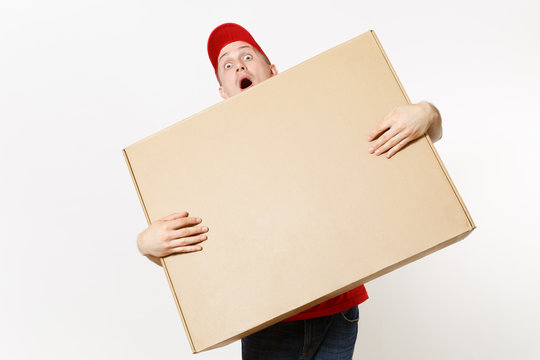 Delivery man in red uniform isolated on white background. Male in cap, t-shirt, jeans working as courier or dealer holding big large heavy empty blank cardboard box. Receiving package. Copy space area
