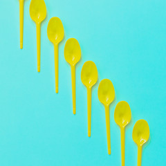 yellow plastic spoons in line on turquoise background. minimal art