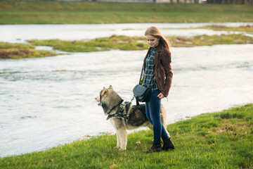 A girl is walking with a dog along the embankment. Beautiful Husky dog. The river. Spring